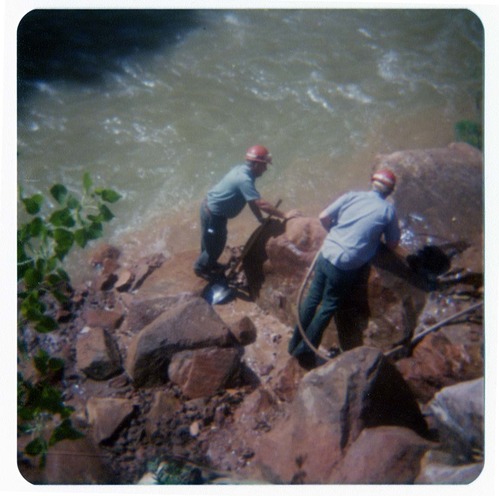 Two men clearing rubble from banks of Virgin River, in anticipation of constructing abutment for new Grotto footbridge.