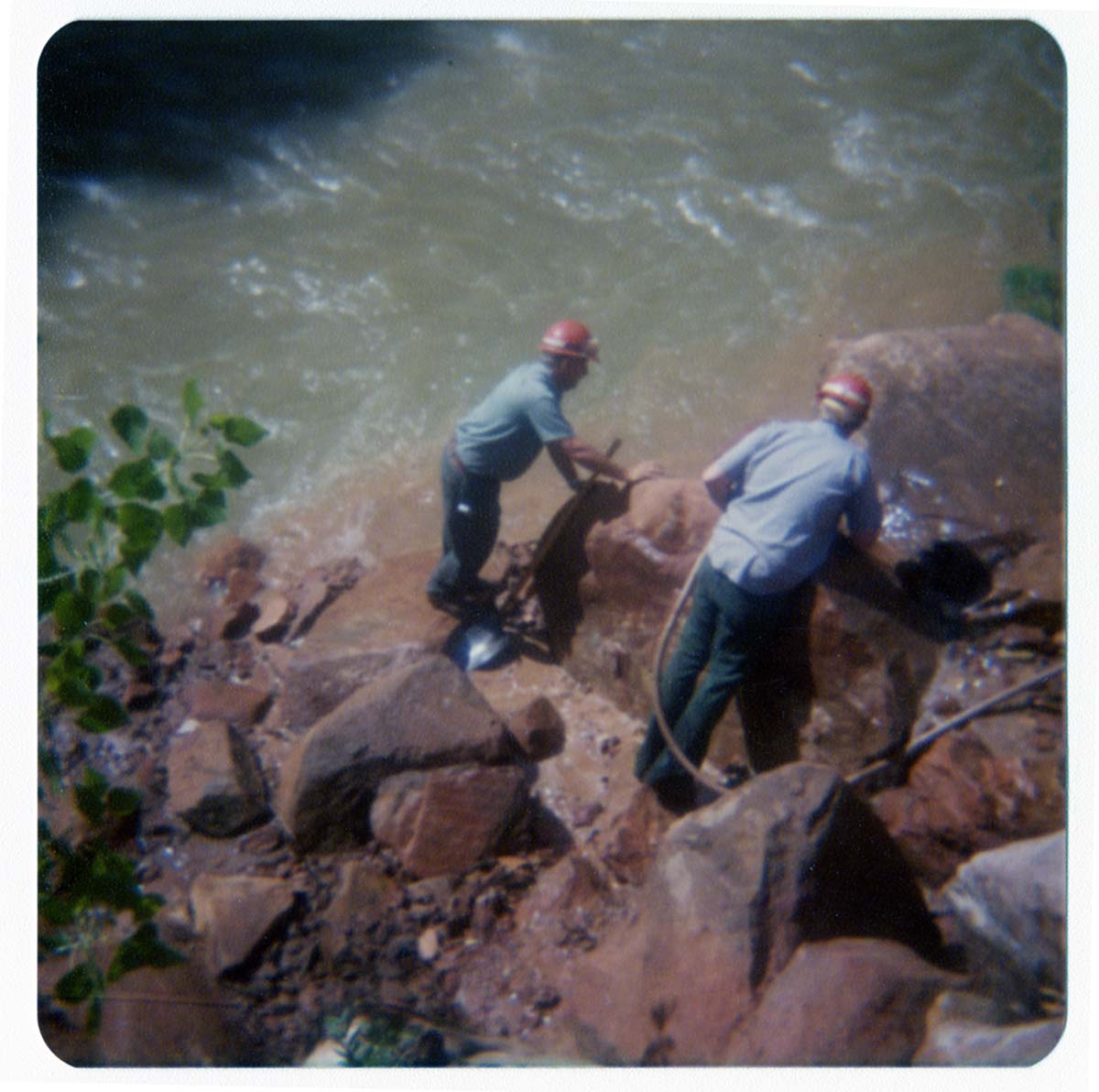 Two men clearing rubble from banks of Virgin River, in anticipation of constructing abutment for new Grotto footbridge.