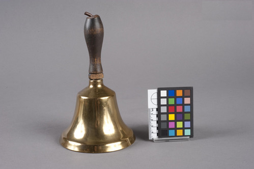 BRASS SCHOOL BELL (a) WITH WOODEN HANDLE (b), UNATTACHED.  IRON ROD EXTENDS FROM END OF HANDLE, THROUGH IT TO CURVED END THAT HOLDS AN IRON BALL CLAPPER INSIDE BELL.  USED BY MISS JULIA COLEMAN AT PLAINS HIGH SCHOOL TO SIGNAL CHANGE OF CLASSES, 1930-40s.