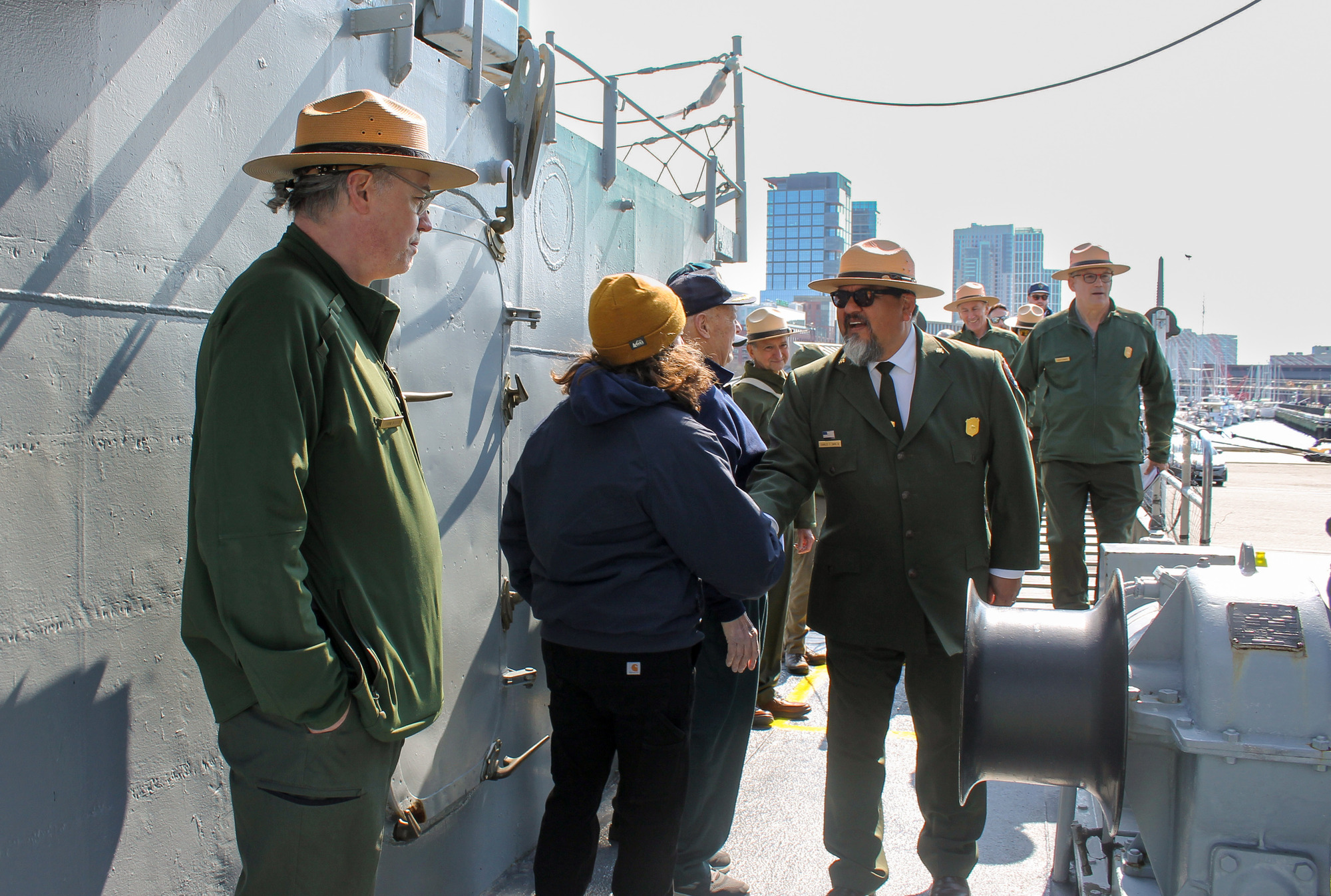 Director Sams abourd USS CASSIN YOUNG; he is shaking hands with a volunteer and surround by other volunteers and park staff.