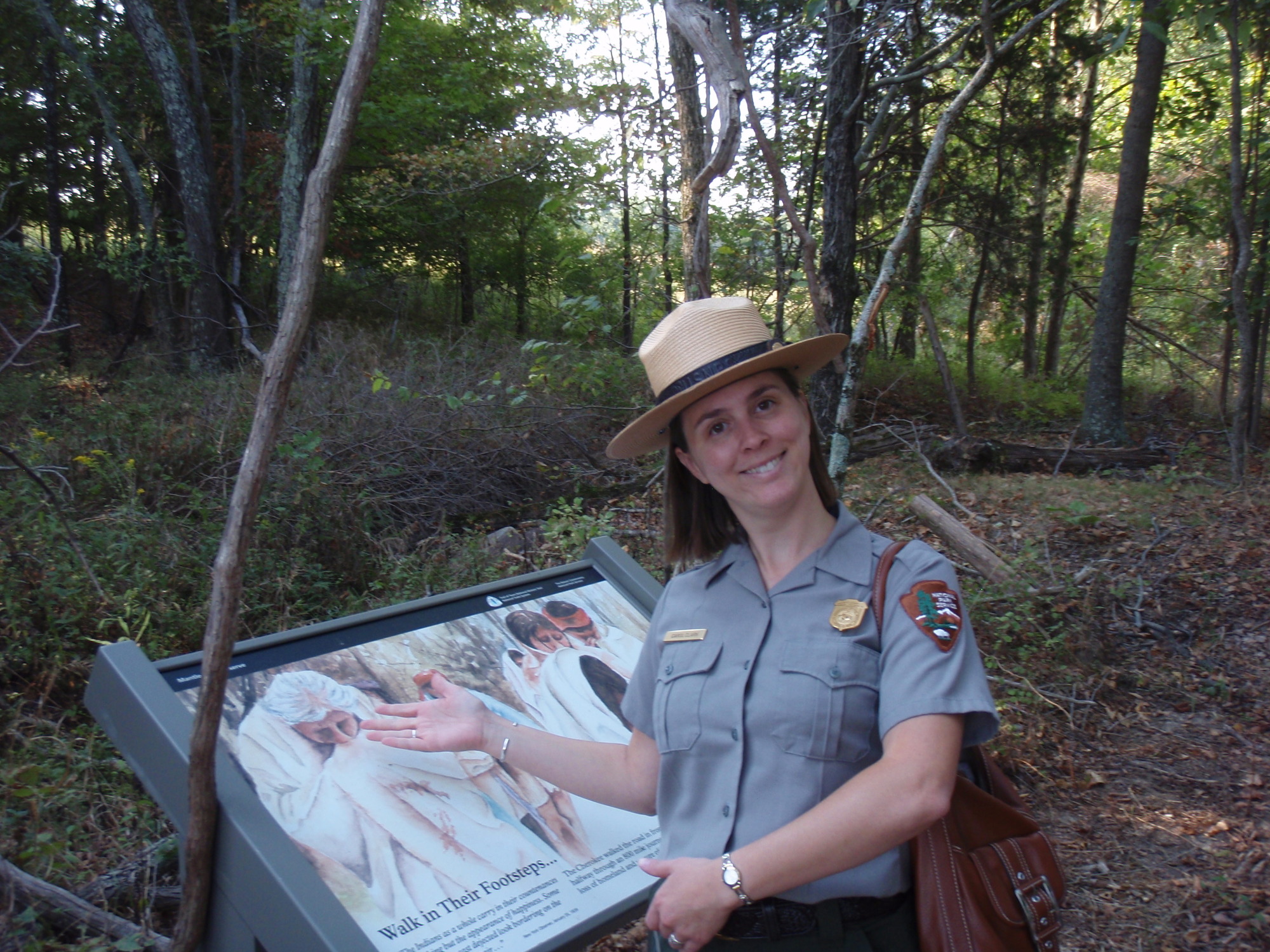 A woman wearing a hat in a wooded area.