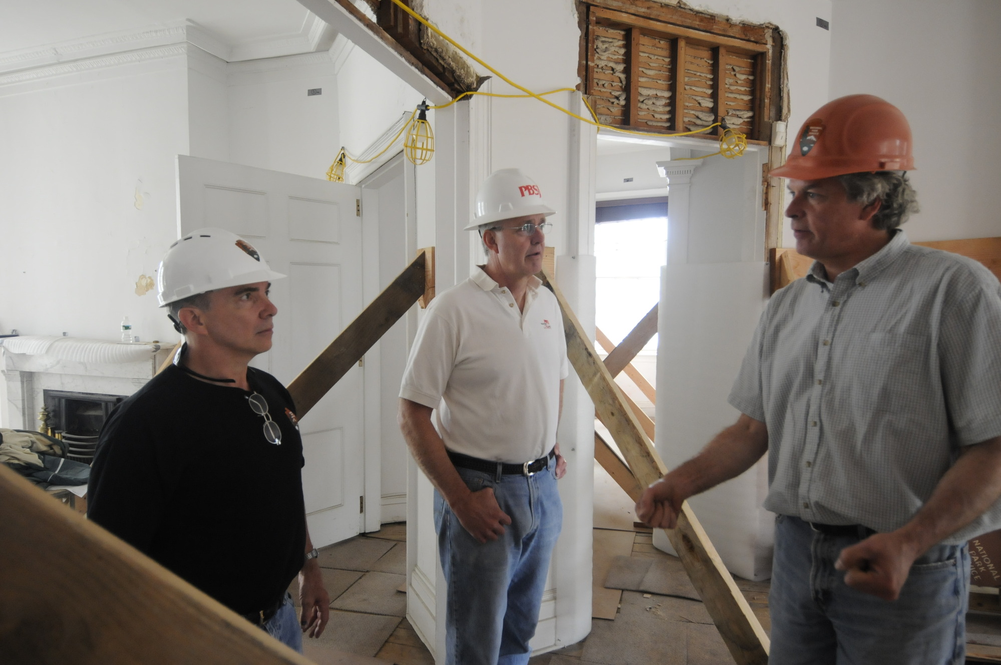 Three people in a room talk in hard hats.