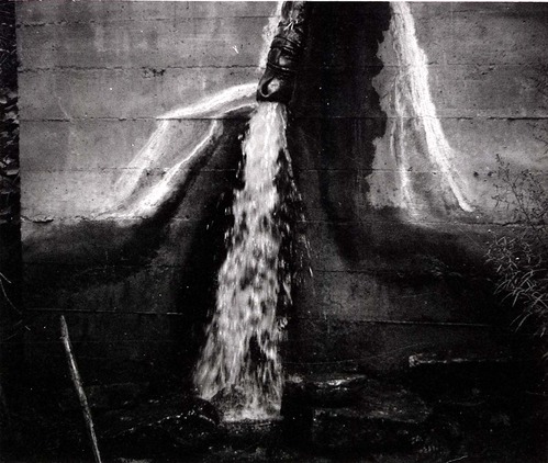 Water pouring on ground from pipe out of cement water tank.