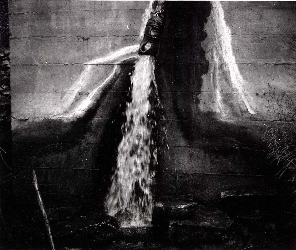 Water pouring on ground from pipe out of cement water tank.