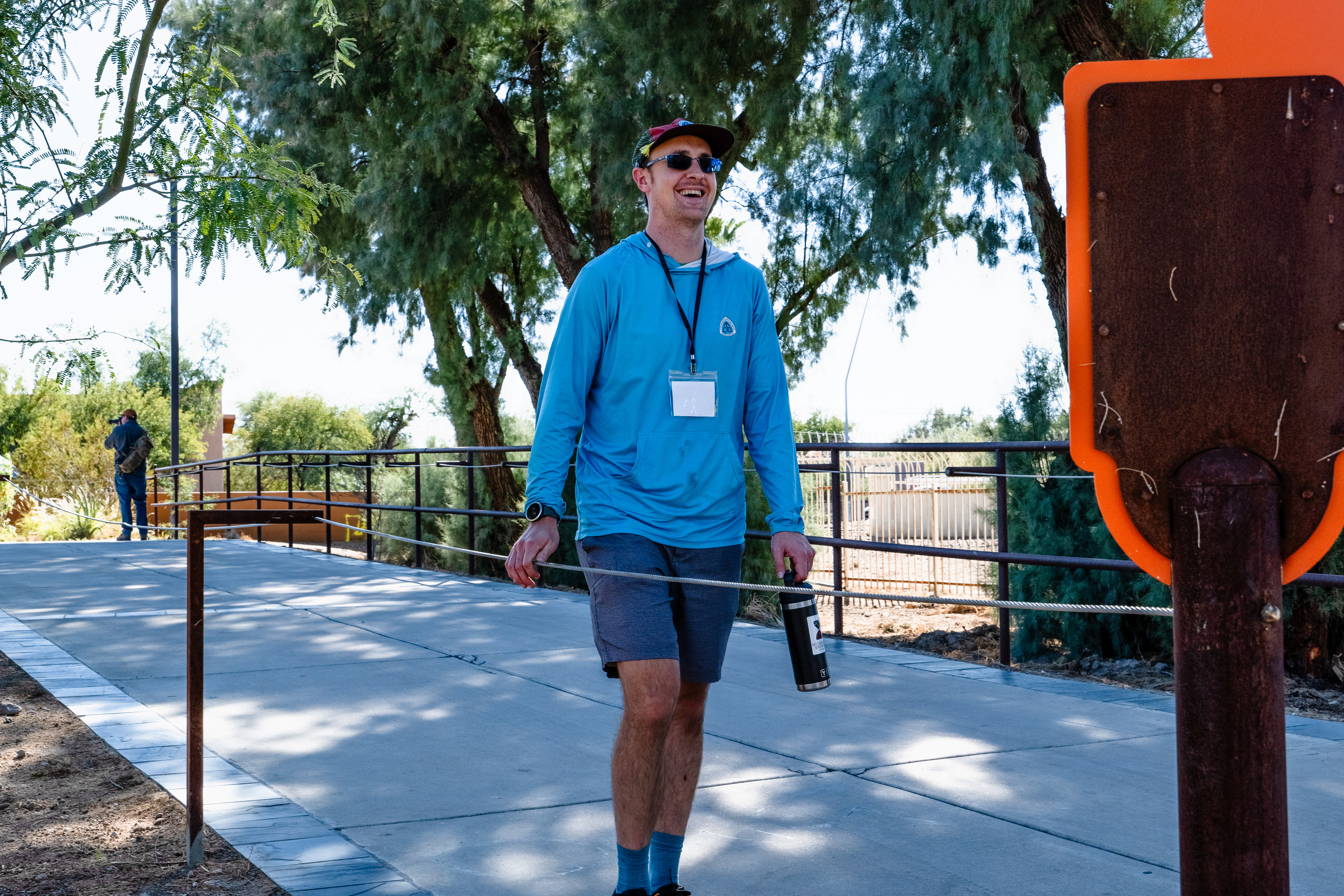 A man smiles as he walks down a pathway holding onto a cord for navigation