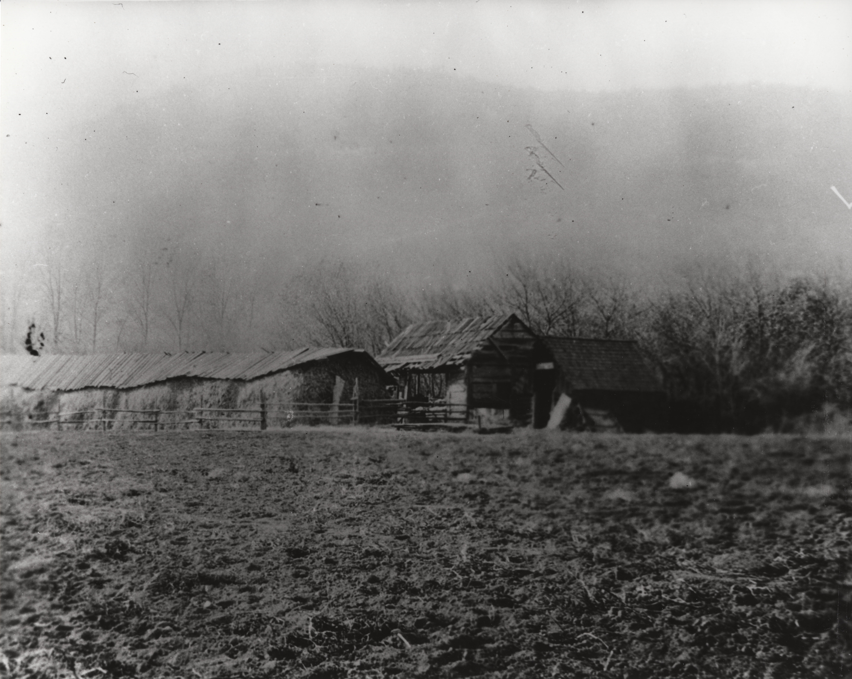 Black and white photograph of single story wooden structure at the edge of a field