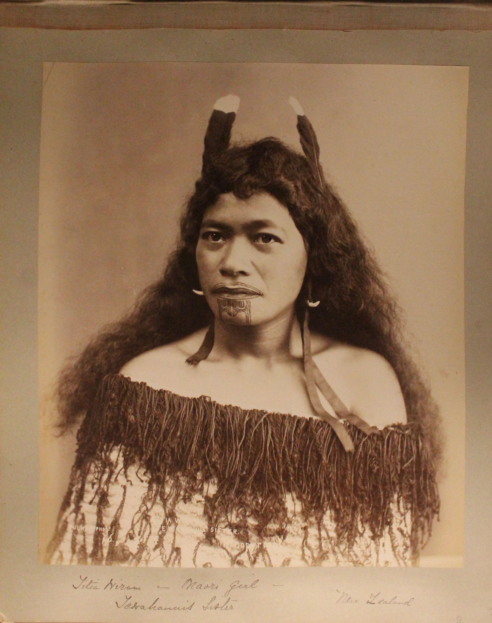 Portrait of Maori girl in traditional outfit with tattoos on her chin.