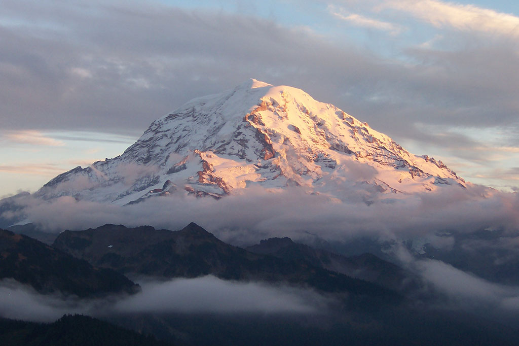 a snowy mountain peak with clouds at the base 