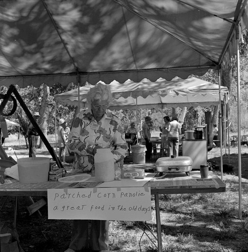 Woman demonstrates making parched corn at the annual first annual Folklife Festival, Nature Center at Zion National Park, September 1977. Sign reads: Parched Corn Panolie, a great food in the old days.