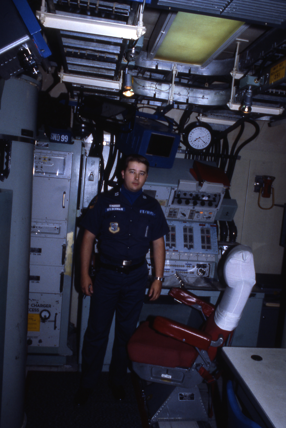 An officer stands at the end of a narrow room in front of a tall electronics console.