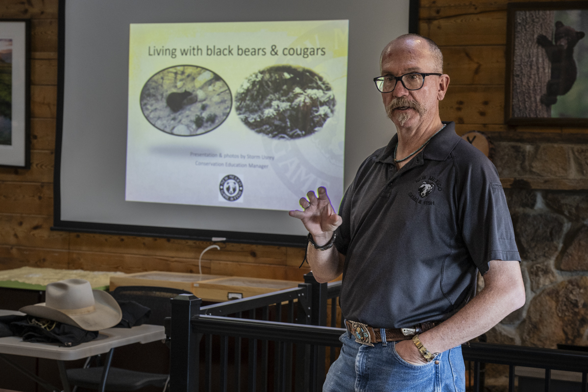 A man stands in front of a projected slideshow and talks to a seated audience.