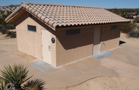 A small tan building with a shingled roof. A paved pathway circles the building. 