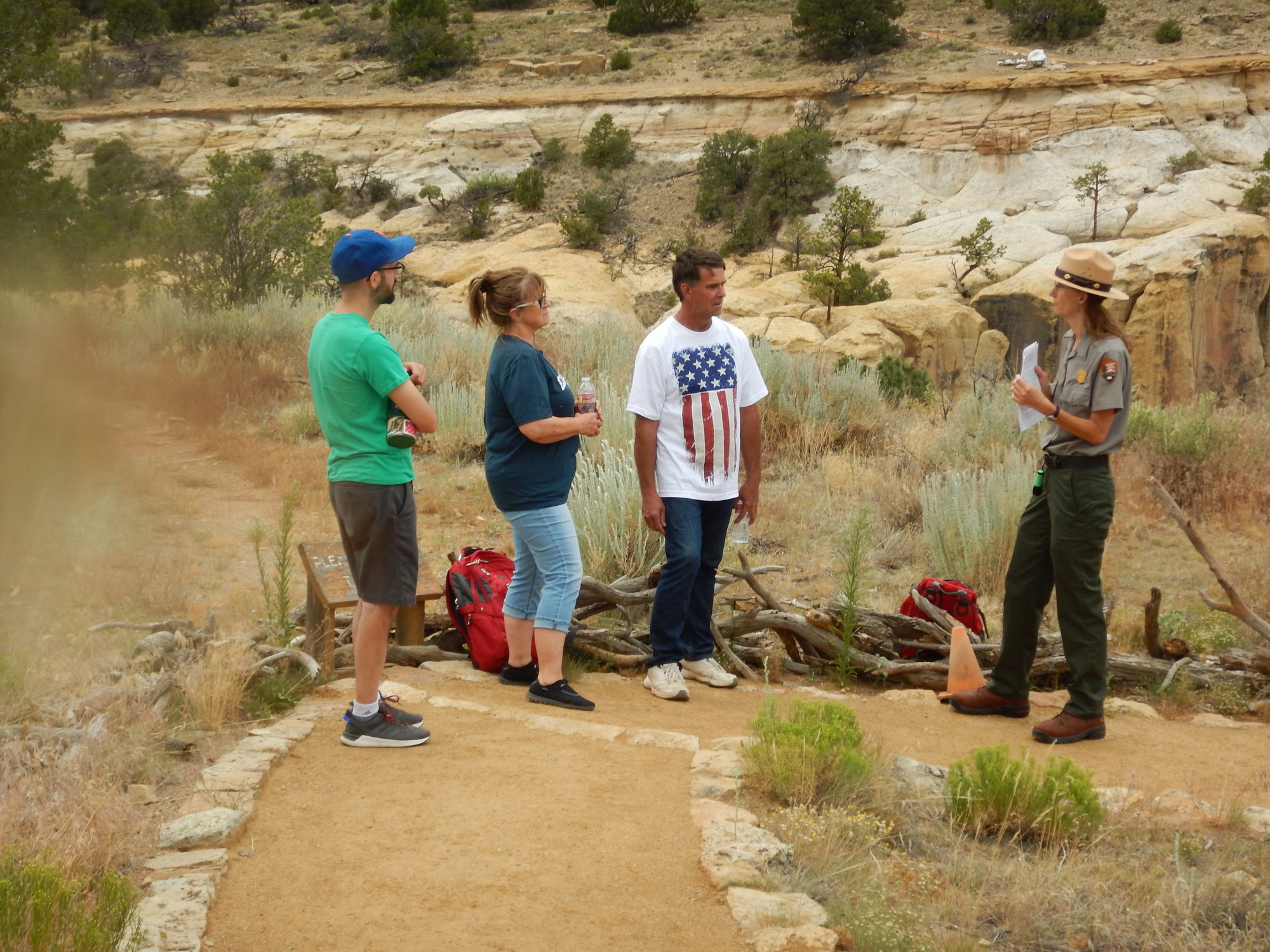 A female ranger holds a paper and talks to three visitors on the headland trail, 