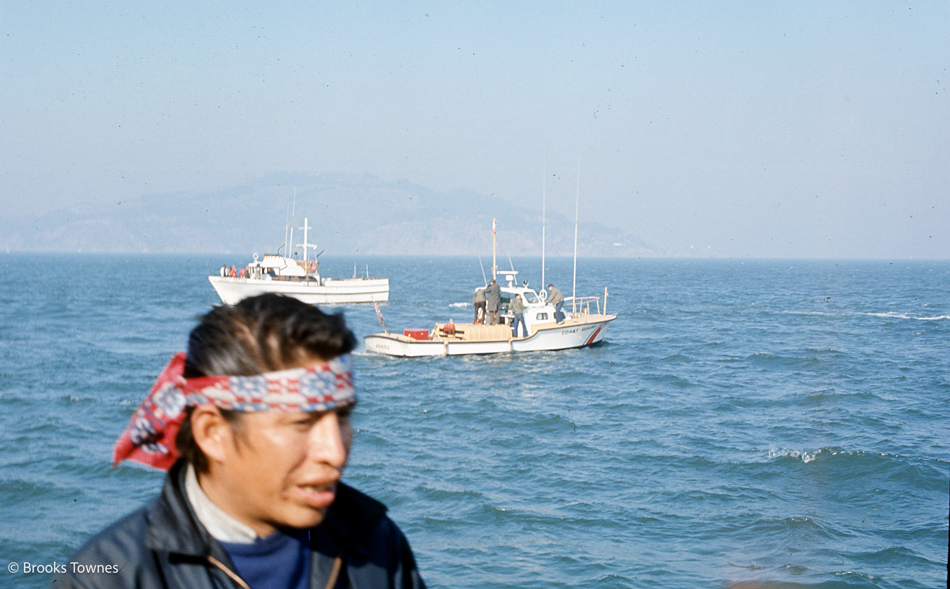 Indian occupier wearng headband in foreground with Coast Guard boat idling behind a short distance away