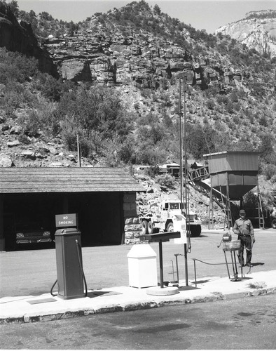 BW Photos of man standing next to maintenance equipment. Vehicle fuel pumps in foreground, equipment and dry sand hopper in background.