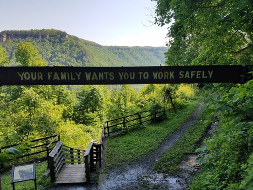 mine safety sign encouraging miners to work safely stands over a hiking trail. 
