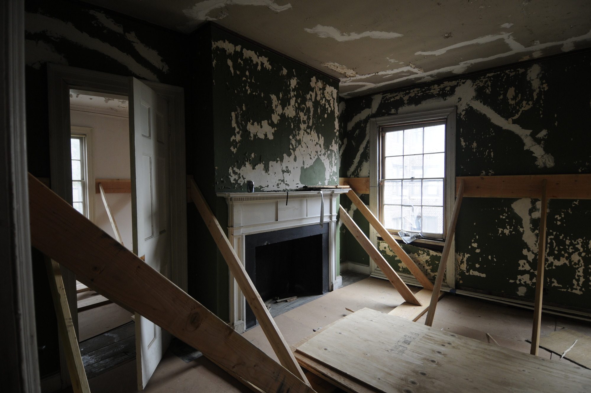 A splotchy green and white room contains planks on the wall that are supported by beams from the floor to the wall.