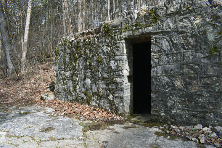 A limestone facade in the woods with an open door. The entrance of the cave is inside.