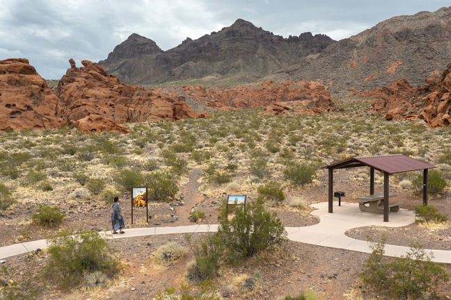 walking trail and picnic shelter lower, red sandstone geologic formations center, mountains in distance