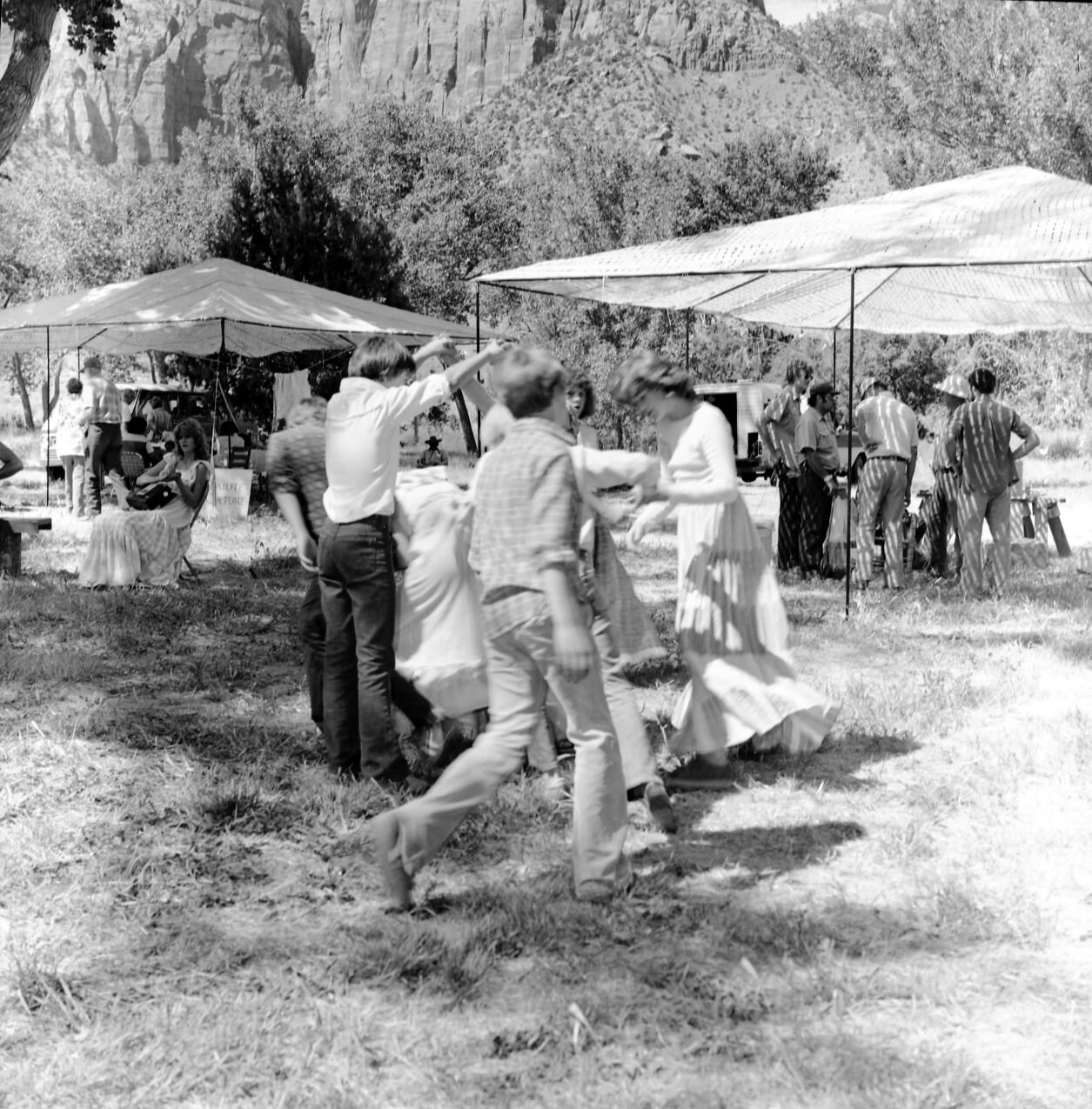 Springdale elementary school children perform a square dance under the direction of Principal Leon Lewis at third Folklife Festival at Zion National Park Nature Center. Jim Fraley, Joe Serna, Jim Felton (with pith helmet) and visitors in background. [No photo or positive. Fingerprints on the negative.]