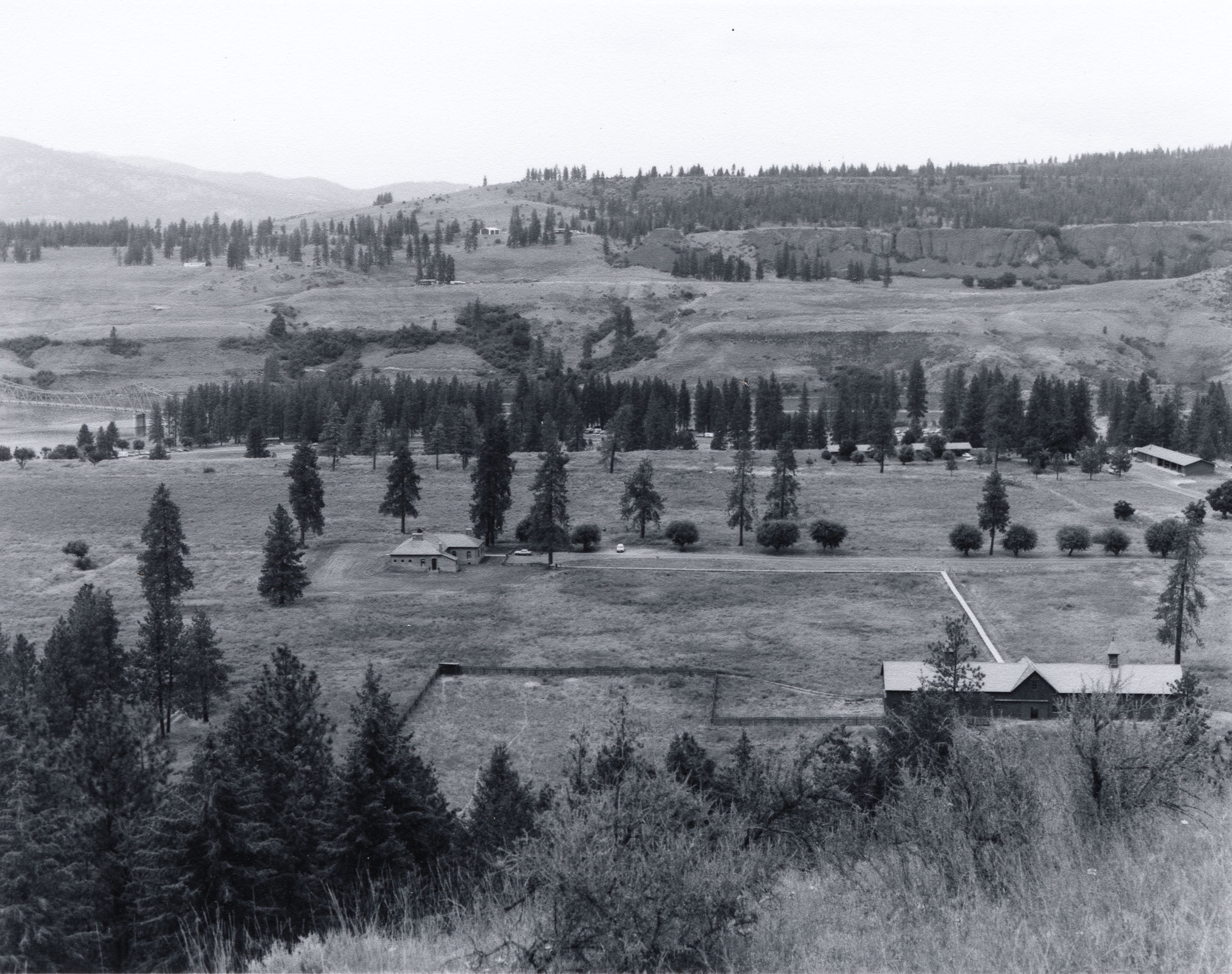 Black and white photograph of valley with buildings in a large clearing