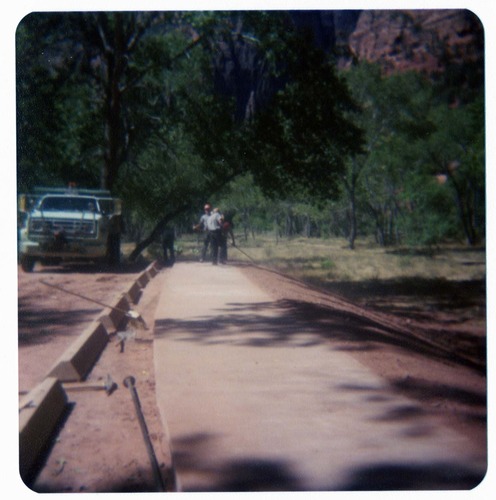 Men working on parking area and sidewalk near the new Grotto footbridge.