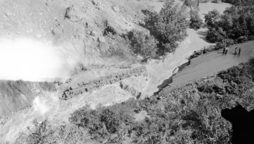 The May 14, 1941 landslide in Zion Canyon just below Birch Creek and Court of the Patriarchs. Landslide from the west bank of the Virgin River caused the stream to undercut the park road and remove a section of it. Note water flow behind the retaining wall and several people standing on the road. [Safety film copy of an original nitrate negative. See catalog numbers ZION 13263, ZION 13264, and ZION 13266 for related images.]