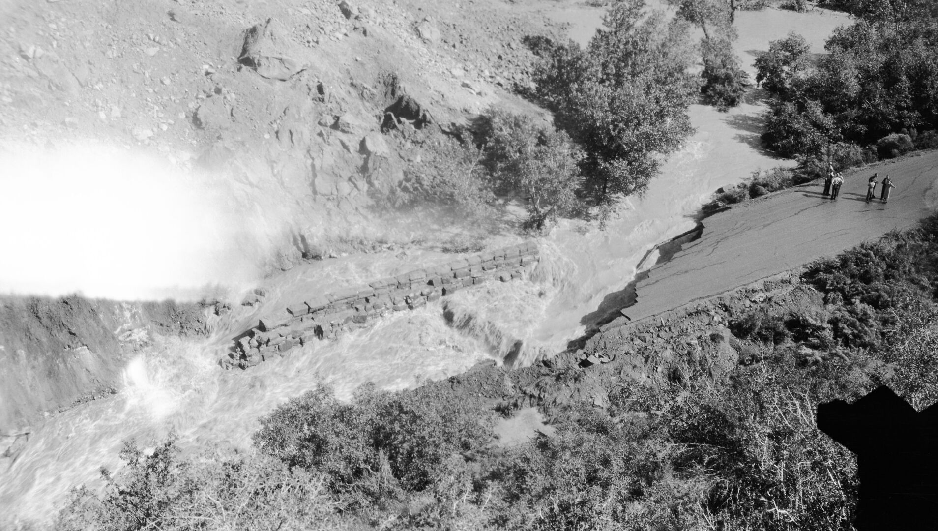 The May 14, 1941 landslide in Zion Canyon just below Birch Creek and Court of the Patriarchs. Landslide from the west bank of the Virgin River caused the stream to undercut the park road and remove a section of it. Note water flow behind the retaining wall and several people standing on the road. [Safety film copy of an original nitrate negative. See catalog numbers ZION 13263, ZION 13264, and ZION 13266 for related images.]
