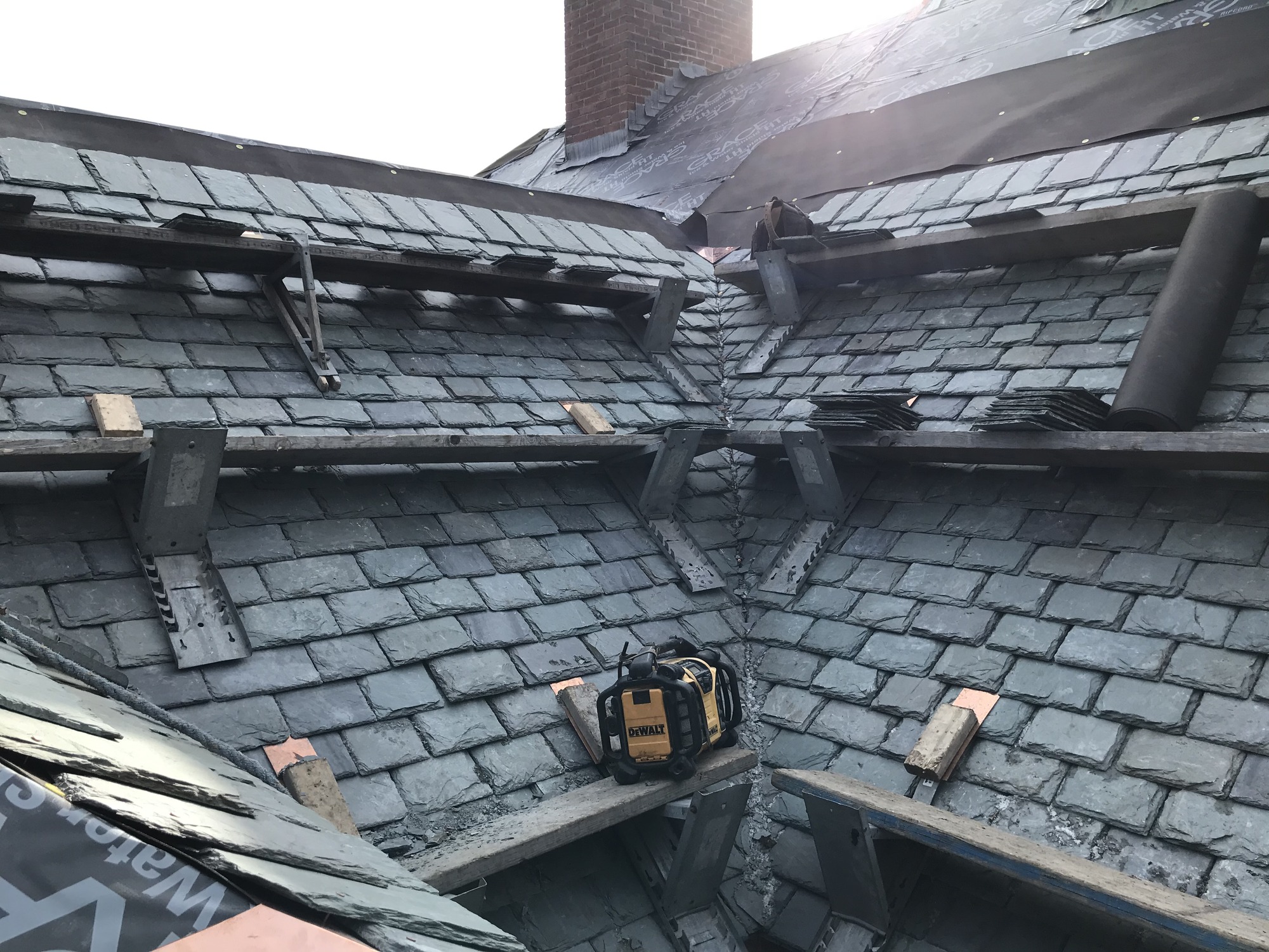 looking at an inside corner of a roof with scaffolding horizontally running across the roof, upper roof tiles removed