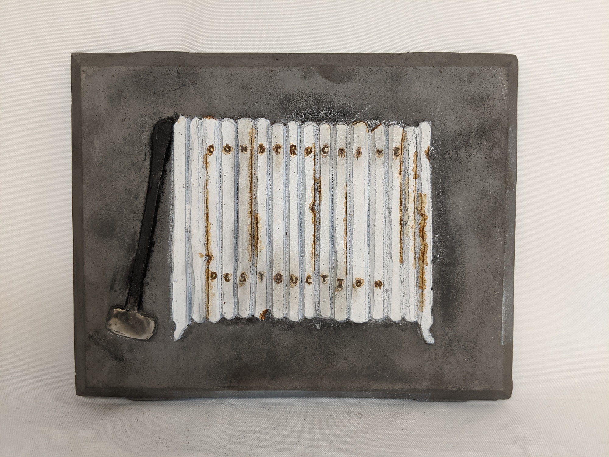 An iron plaque with a white radiator and sledge hammer with the words "constructive destruction."