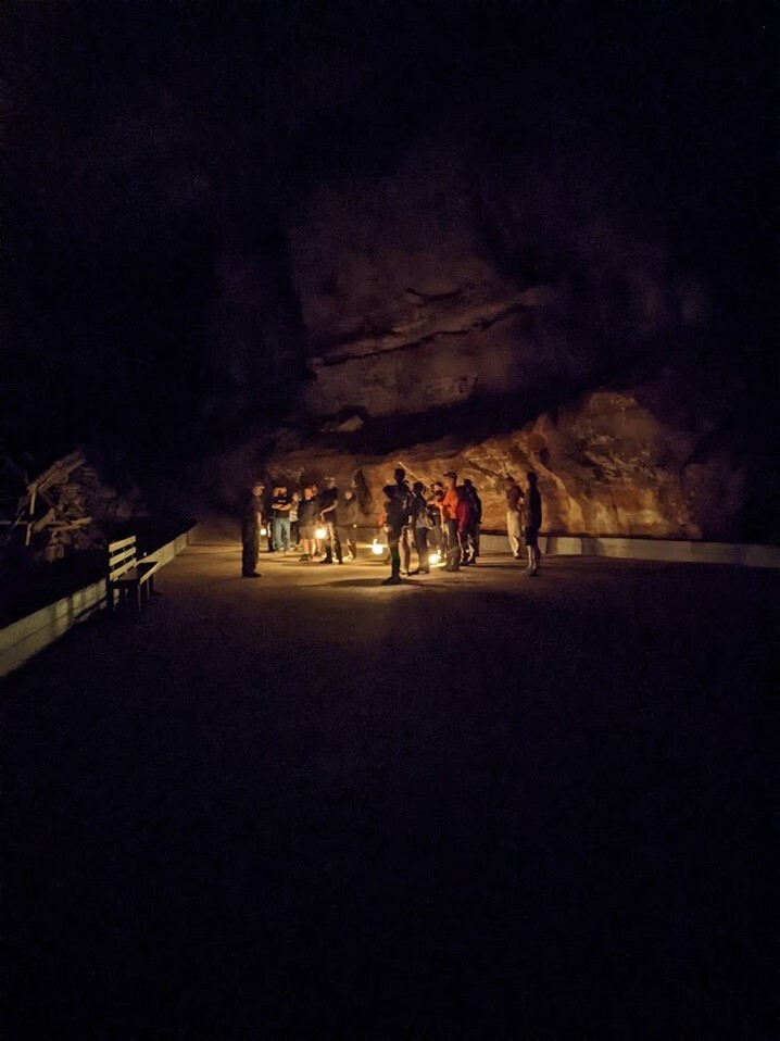 Small group of people holding lanterns inside large cave.