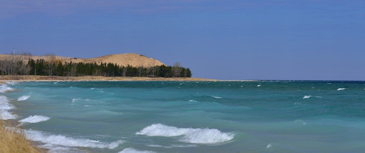 Take a mental hike as you consider Lake Michigan waves gently rolling the shore along a deserted lakeshore. A sand dune sits quietly in the distance with trees at its base.  