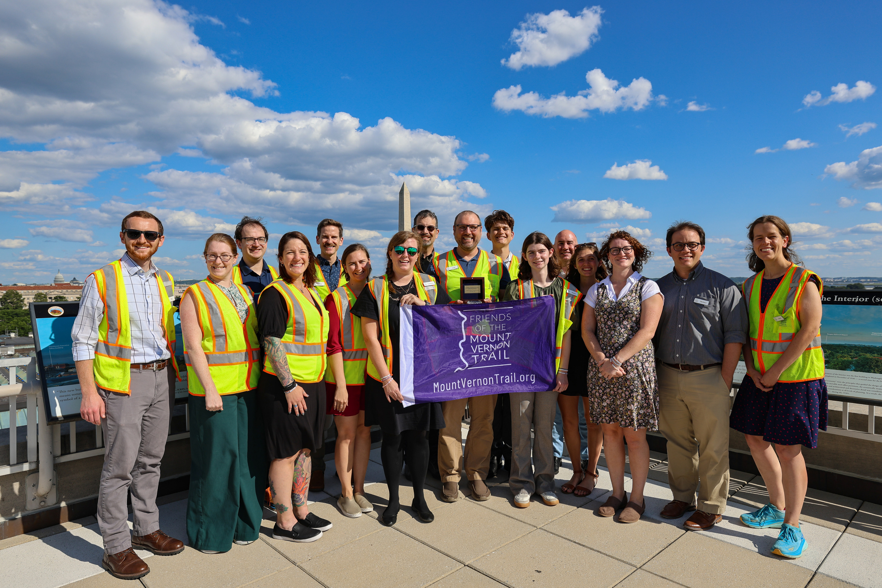 A group of award recipients in a yellow vests pose for a photo on a rooftop.