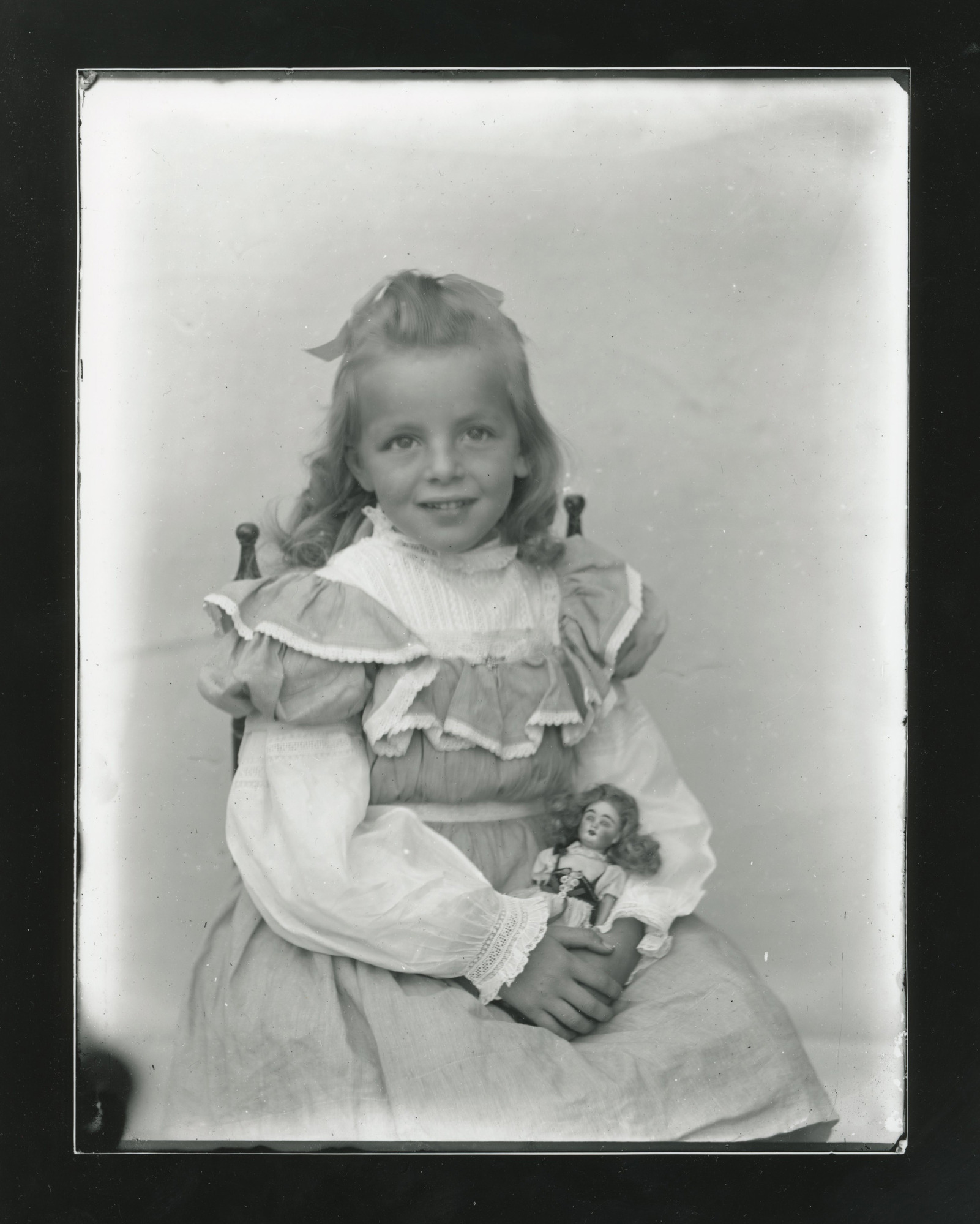 A young white girl sits in a small chair and holds a small white doll in her lap.