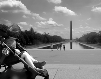 A little girl in a stroller looks over at the Washington Monument. The photo is in black and white. 