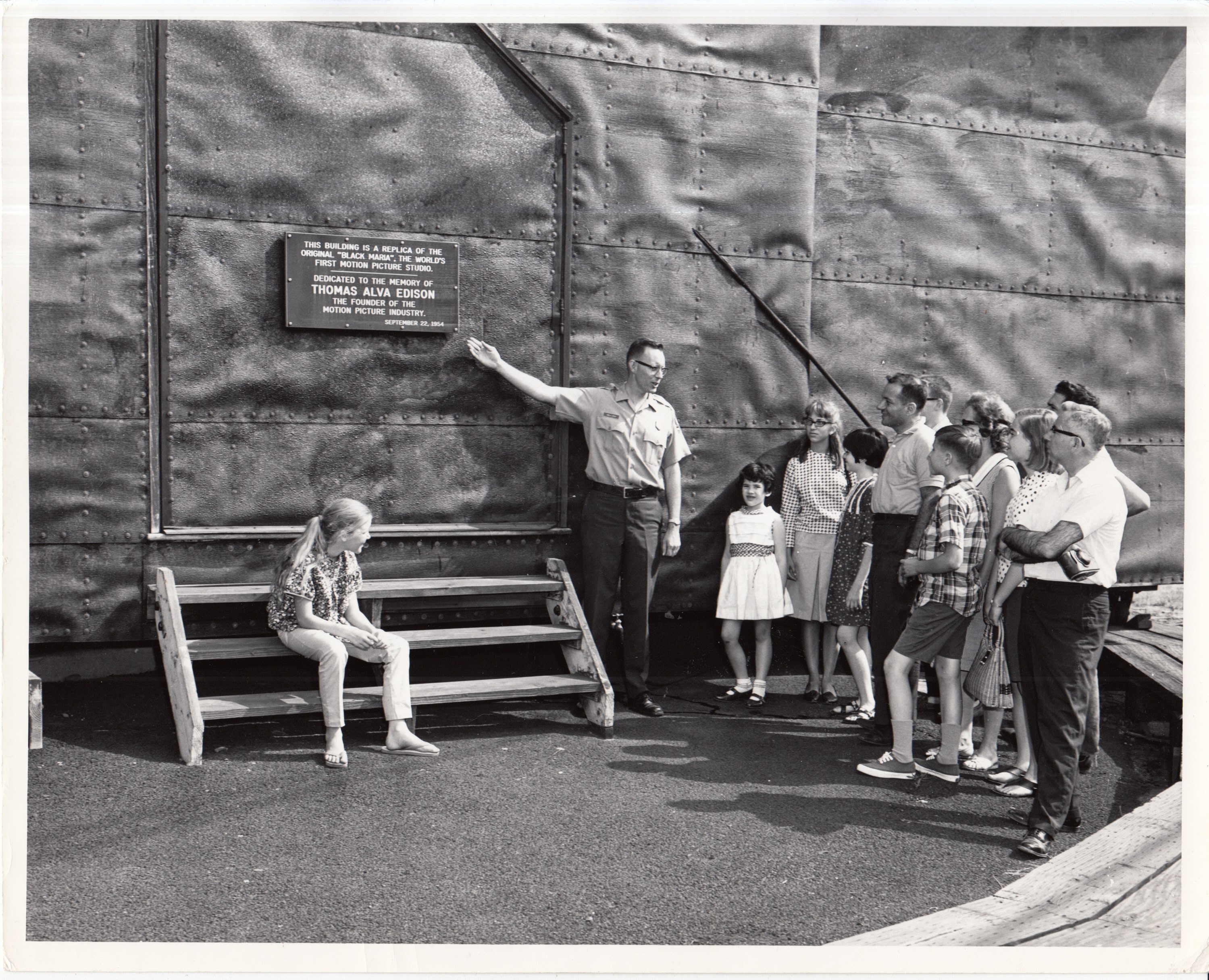 Tour group outside replica of Black Maria, park guide pointing to plaque on door of building.
