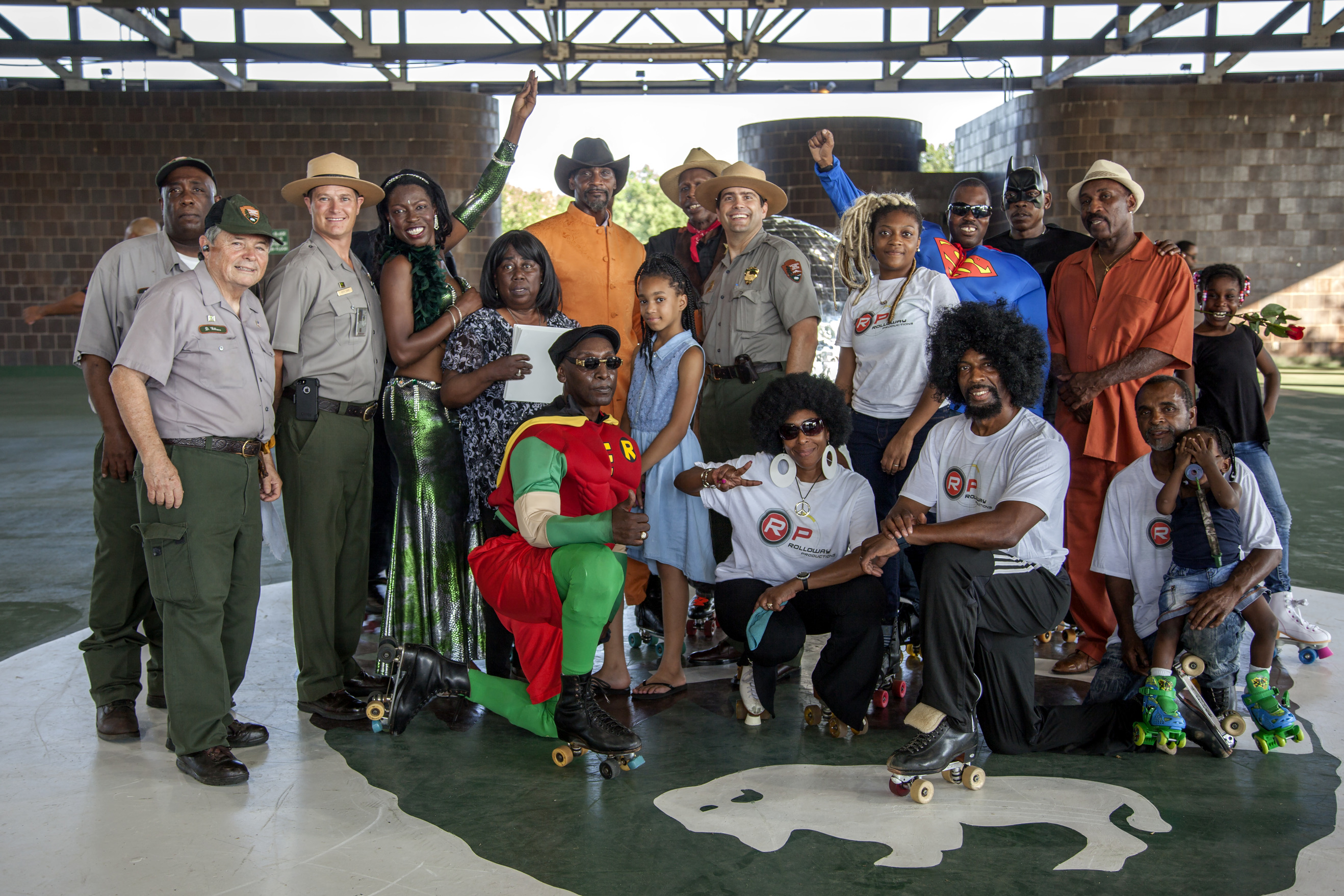 A group of visitors dressed in 1970s attire and super hero costumes pose with park rangers at the  Anacostia Park Roller Skating Pavillion 