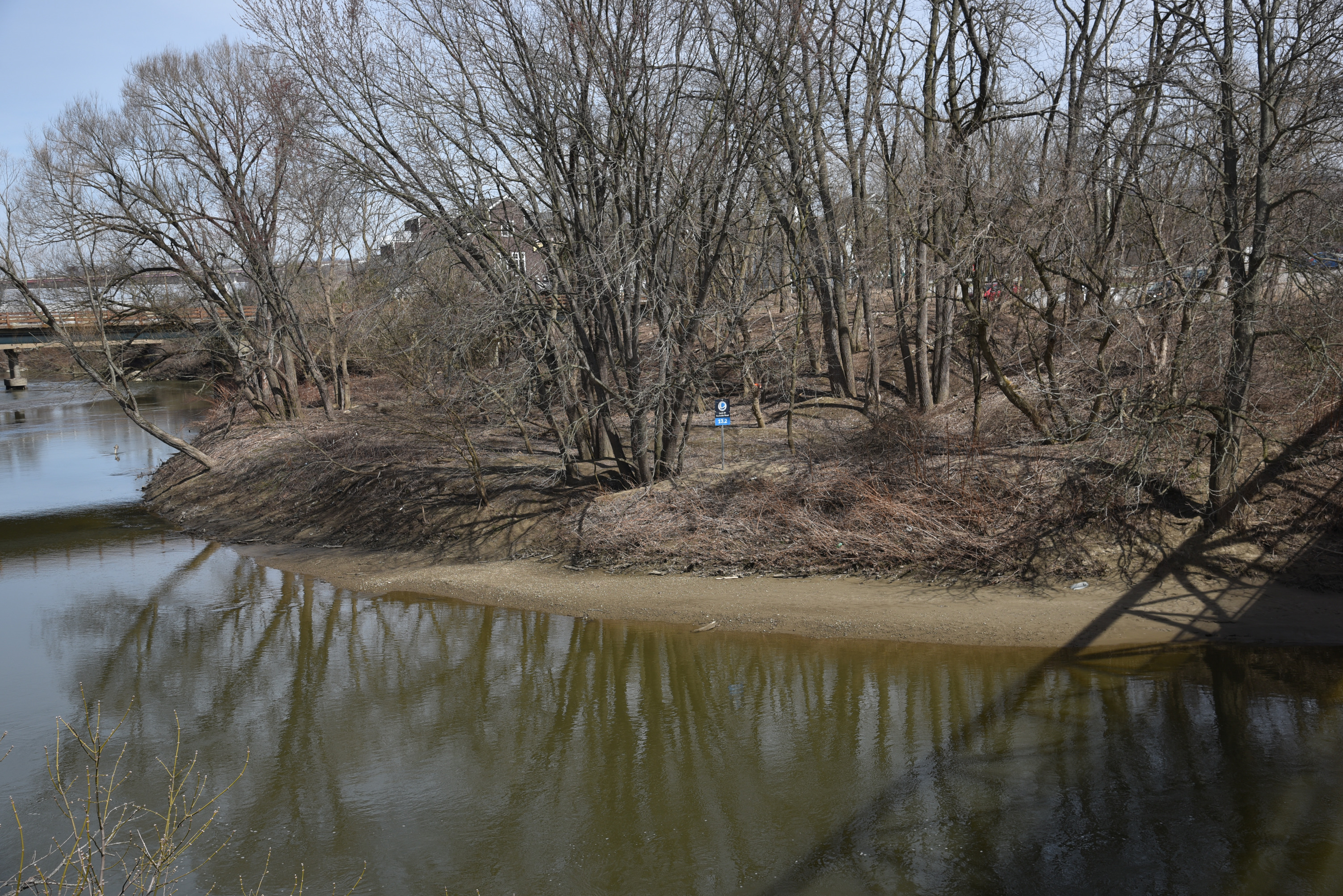 View of the Cuyahoga River looking downstream. The Lock 39 river access point can be seen, with a Cuyahoga River Water Trail sign seen at the top of the ridge. The shadow of Rockside Station Pedestrian Bridge, which the photo is taken from, can be seen on the river in the lower right corner.