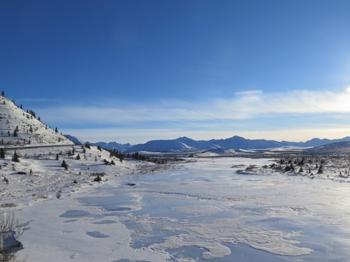 ice covered river dotted with compacted snow in a few areas at the foot of a hill