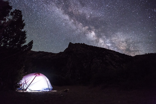 Stars including the Milky Way show above a pop up tent lit from inside.