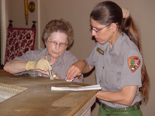 Two NPS personnel using paper towels and soapy solution to clean the top surface of a marble baluster.