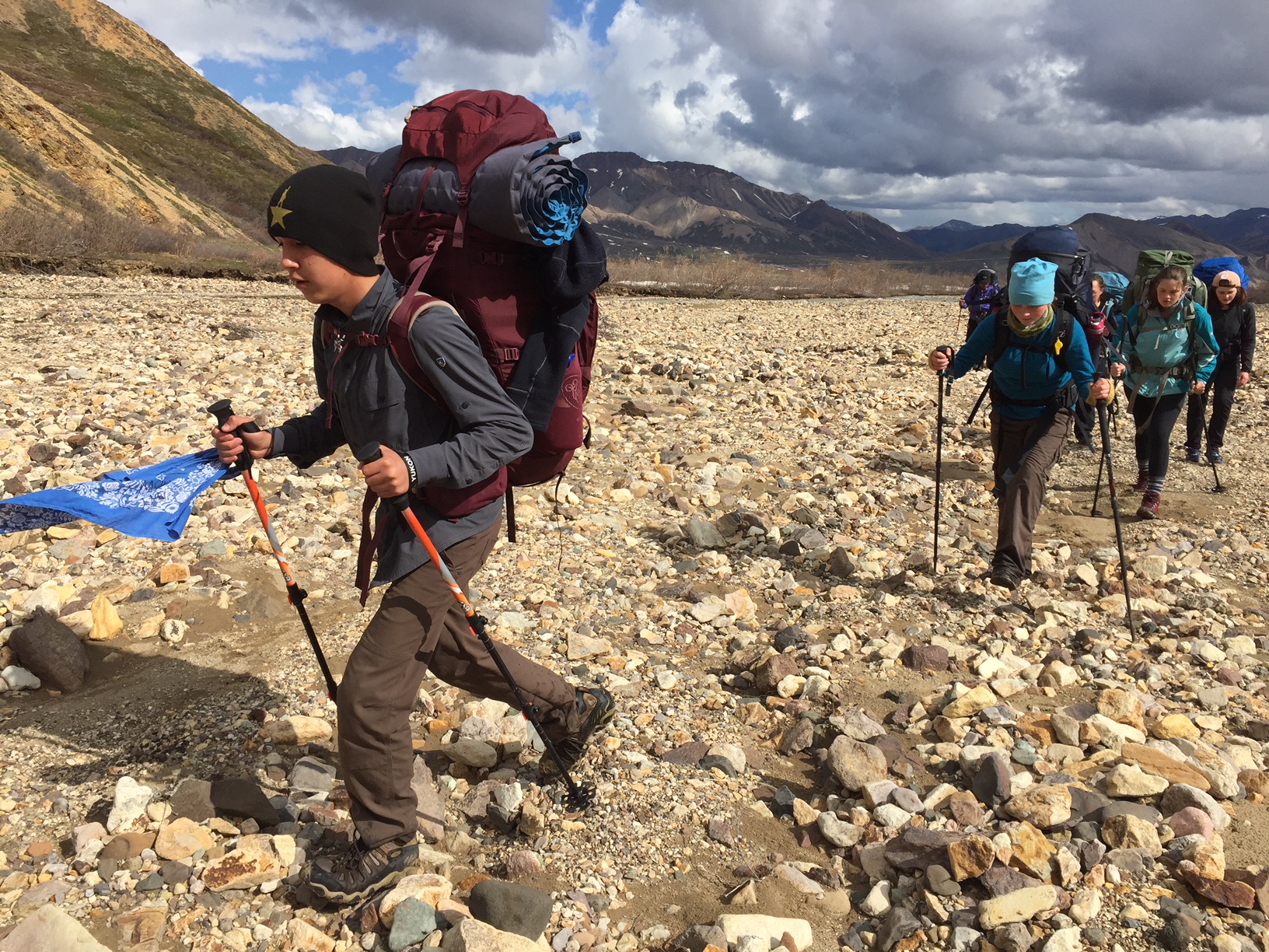 five teens hiking across a gravelly valley