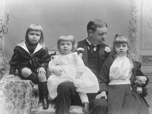 A formal photographic portrait of a man and three small children.