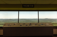 Three large glass windows reveal forested, rolling hills stretching towards the horizon. There is a sign that says 