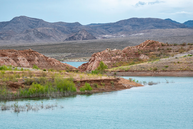 Cove, water foreground, sandy and rocky hills surrounding water, mountains in background