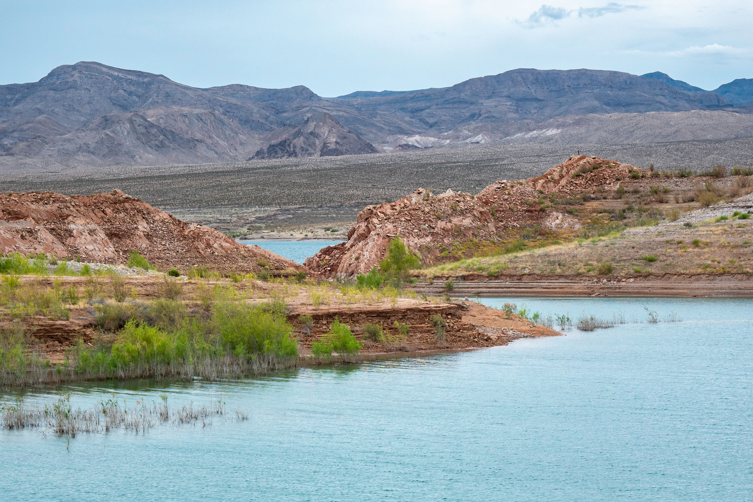 Cove, water foreground, sandy and rocky hills surrounding water, mountains in background