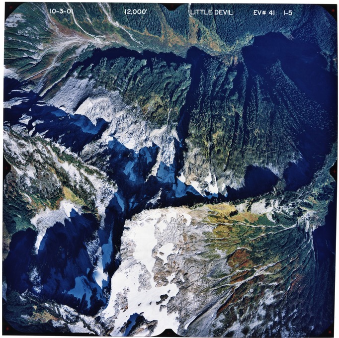 Color aerial photograph of glaciated mountain peak with forested valleys below.