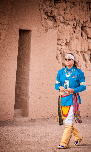 colorfully dressed American Indian musician Arvel Bird walks past the earthern Great House