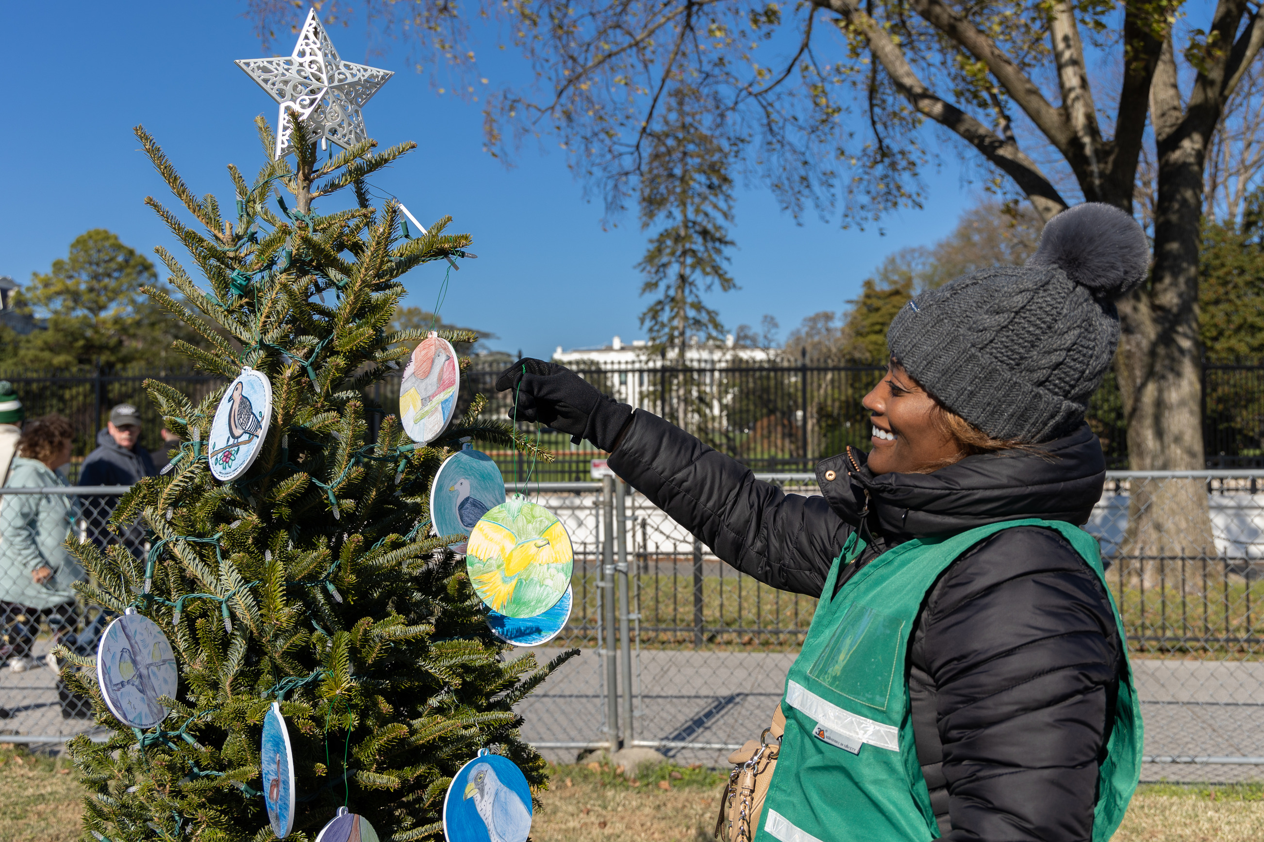 A volunteer hands up hand made ornaments onto a Christmas tree in front of the White House. 