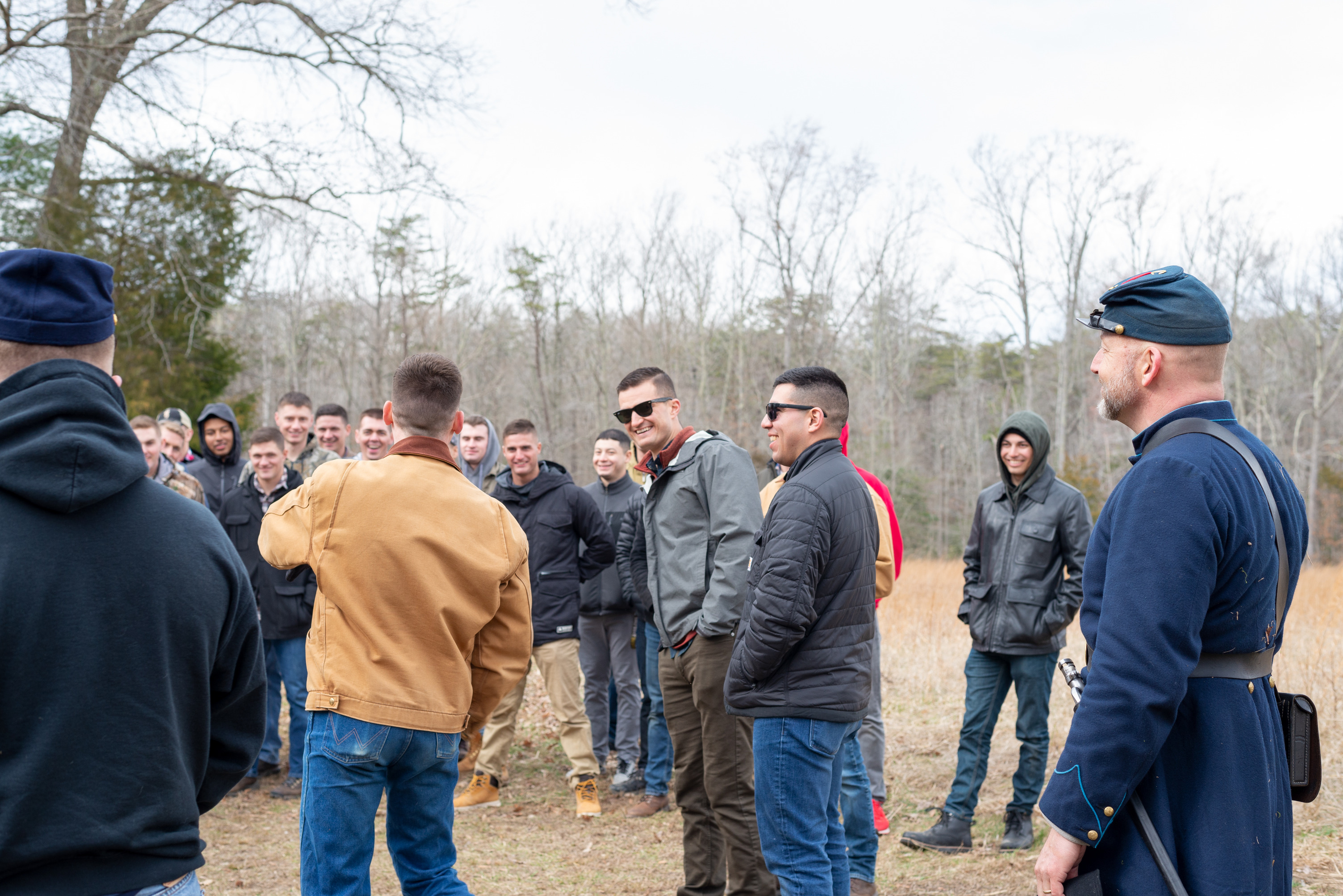 Four men stand in front of a group of people while a man in a Union Civil War uniform looks on in the forefront.